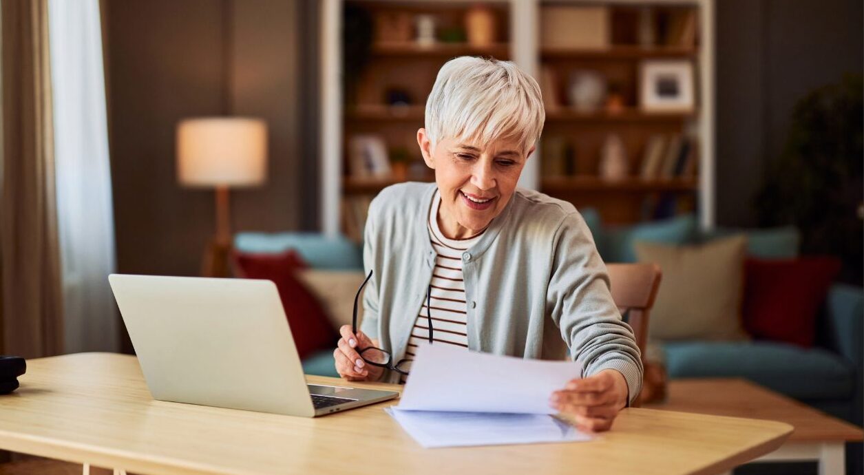 Woman reading report at beside laptop in home setting